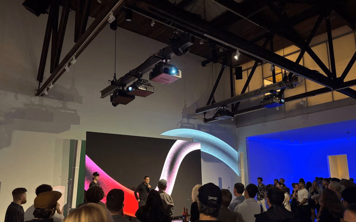 Photo from a Krea launch event showing a large presentation screen with an abstract pink-and-blue gradient animation, addressed by a speaker in front of an audience.