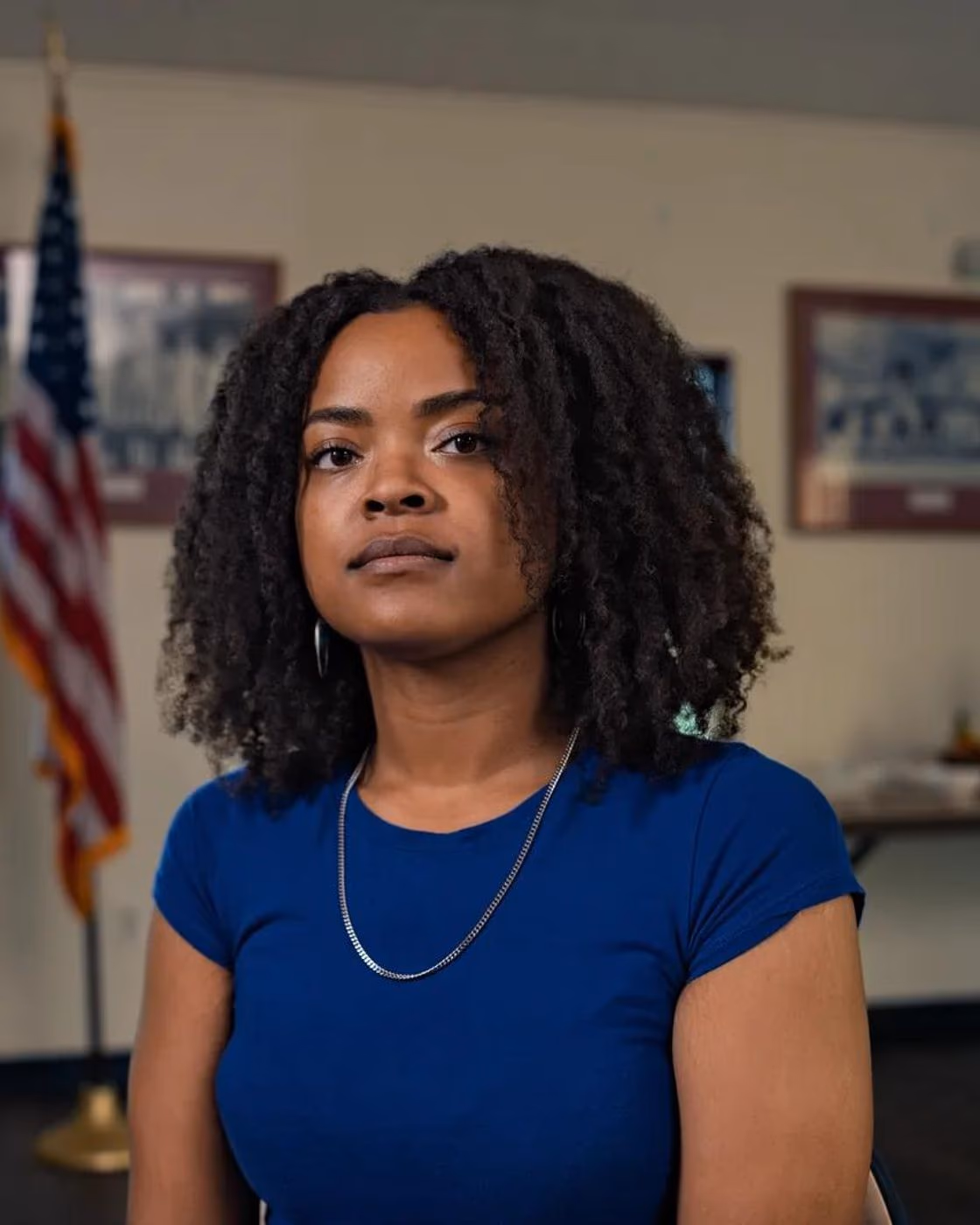 Portrait of one of the real people interviewed for Anthropic's hard-questions research campaign, seated in front of a US flag.