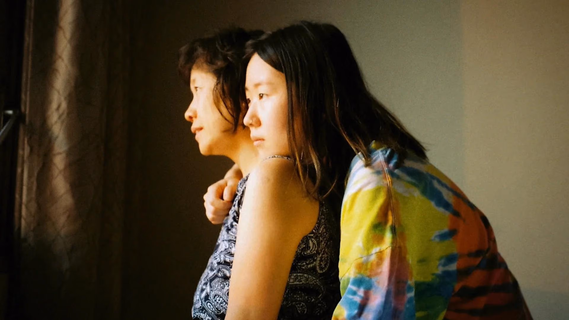 Warm, intimate still photography of two people from Anthropic's 'hope in hard questions' campaign, illustrating the film's grainy, home-movie visual register.