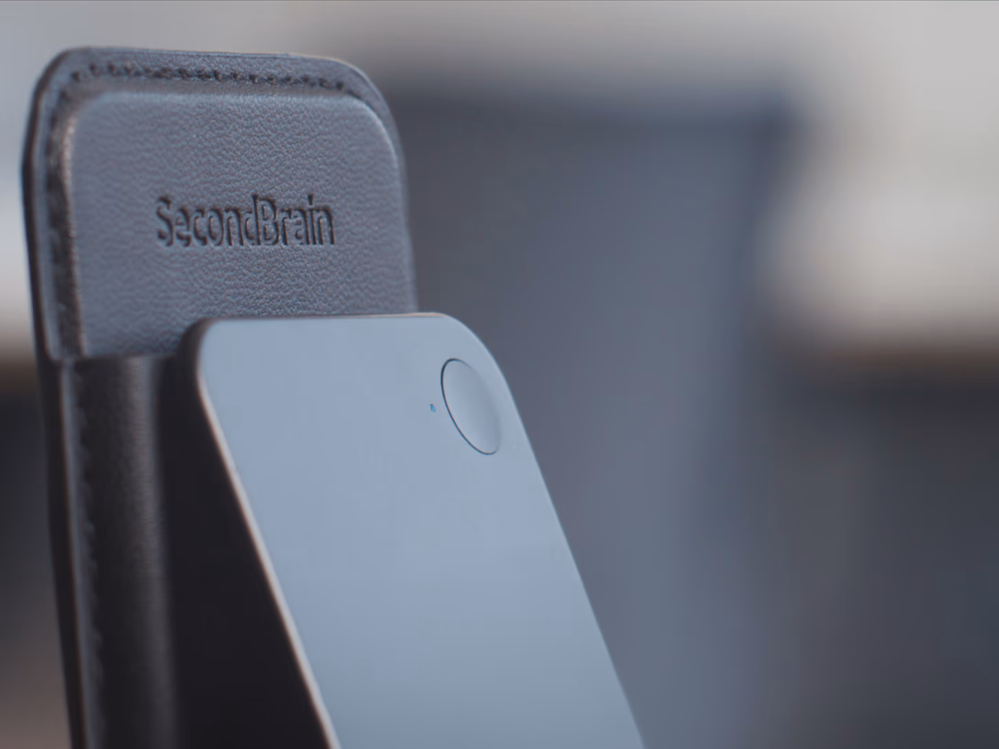 Close-up of the GenSpark SecondBrain Note AI recorder, its aluminium body visible peeking out of its embossed leather MagSafe wallet.